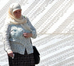 Unha bosníaca musulmá camiña ao carón do muro memorial do Cemiterio de Srebrenica